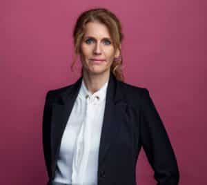 Lena Schelin är generaldirektör på IMY. Porträttbild, vitblus, svart/mörkblå kavaj, står framför mörkrosa/lila bakgrund